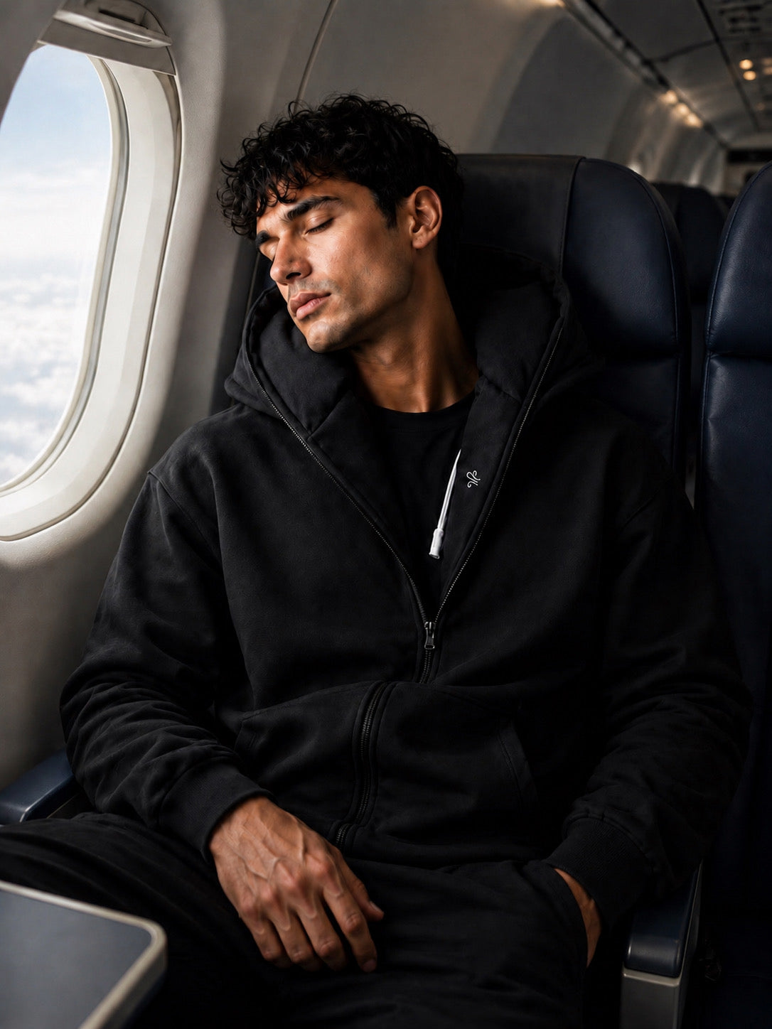 Traveller sleeping comfortably on a plane wearing the KIVO Neck Pillow Hoodie with built-in neck support.